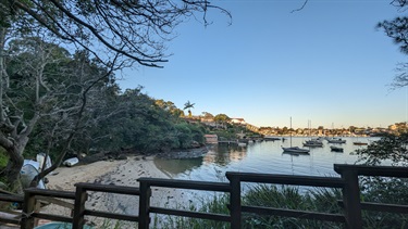 Steps within Betts Park, leading down to a small beach that is visible in the foreground, as well as boats floating in the river in the background.