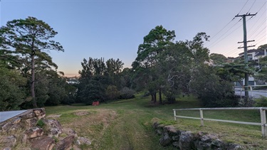 Northern entrance to Betts Park, showing a small rocky drop-off, with grassy areas shaded by trees in the foreground.