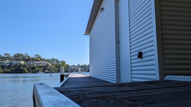 Ferdinand Street Reserve hosts a public boat jetty, photo is low angle and shows the boat shed and the associated jetty sitting along side the Lane Cove River