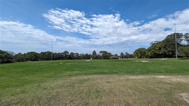 Photo shows a wide angle of the Weil Parks Sports Field. The sun is shining in the sky and there are some light cloud coverage. The perimeter of the park is surrounded by bushland. There is a large crane that can be seen in the far right corner (background).