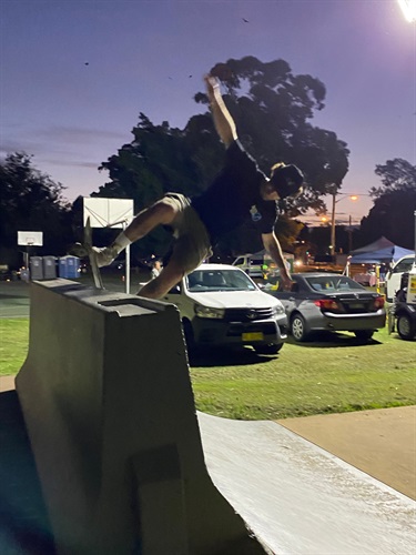 Photo shows a rider at the Gladesville Reserve Skatepark, performing a trick on one of the ramps. he approached the ramp from right to left. He has reached the crest of the ramp and he is pressing his board into a 