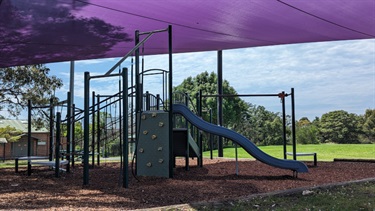 Photo shows the Weil Park Playground, covered by shade sails. There is a slide, a small rock climbing frame and a jungle-gym.