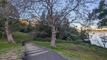Western entrance to Betts Park, showing grassy areas shaded by trees, as well as steps leading down to a small beach.