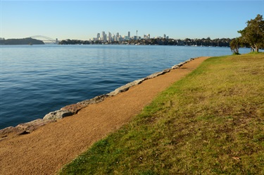 Gravel Footpath flanked by grass, travelling along Sydney Harbour Foreshore with the Sydney Harbour Bridge and city in the background